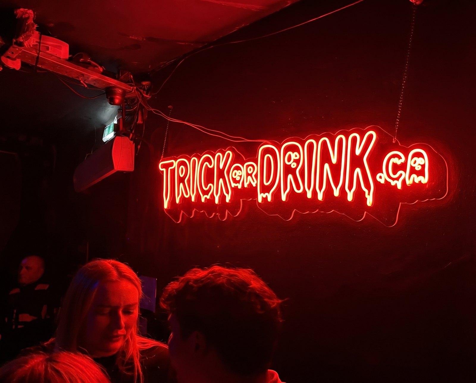 The red Trick or Drink neon sign lit above the crowd at last year's Halloween party